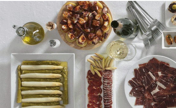 Un surtido de platos que incluye jamón, pulpo a la gallega, espárragos, lomo y fuet, una copa de champán y aceite de oliva