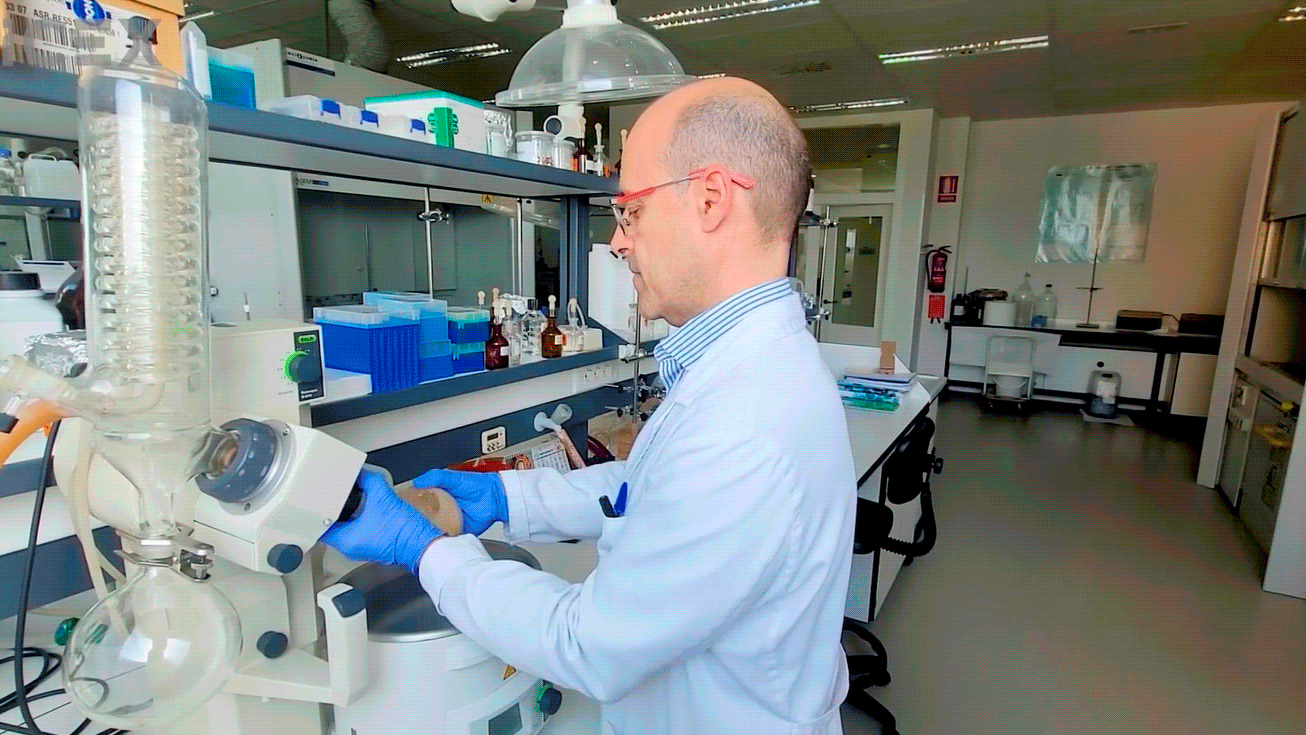 Un trabajador de Biomar vestido con bata y guantes maneja un microscopio