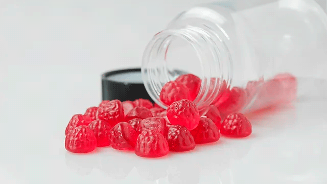 Varias gominolas rojas salen de un tarro de cristal tumbado
