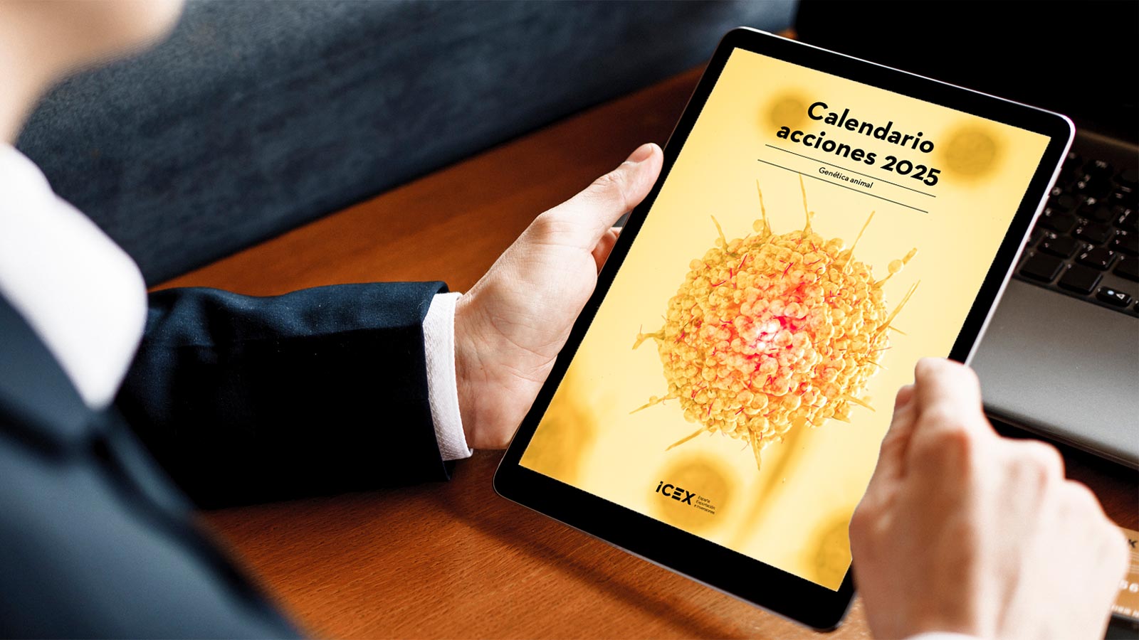 Un hombre con traje azul sujeta una tablet en la que se visualiza la portada del calendario de actividades para el sector de genética animal.