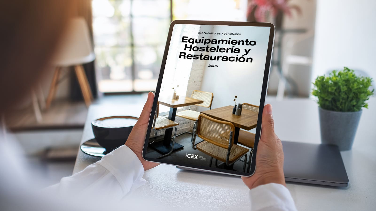 Una persona sostiene con las dos manos una tablet donde visualiza el calendario ICEX de actividades para Horeca 2025