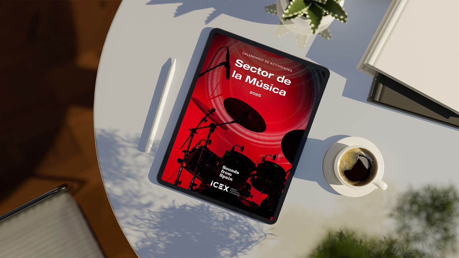Sobre una mesa blanca hay un bolígrafo blanco, una tablet donde se visualiza la portada del calendario ICEX del sector de la música y una taza blanca con café.