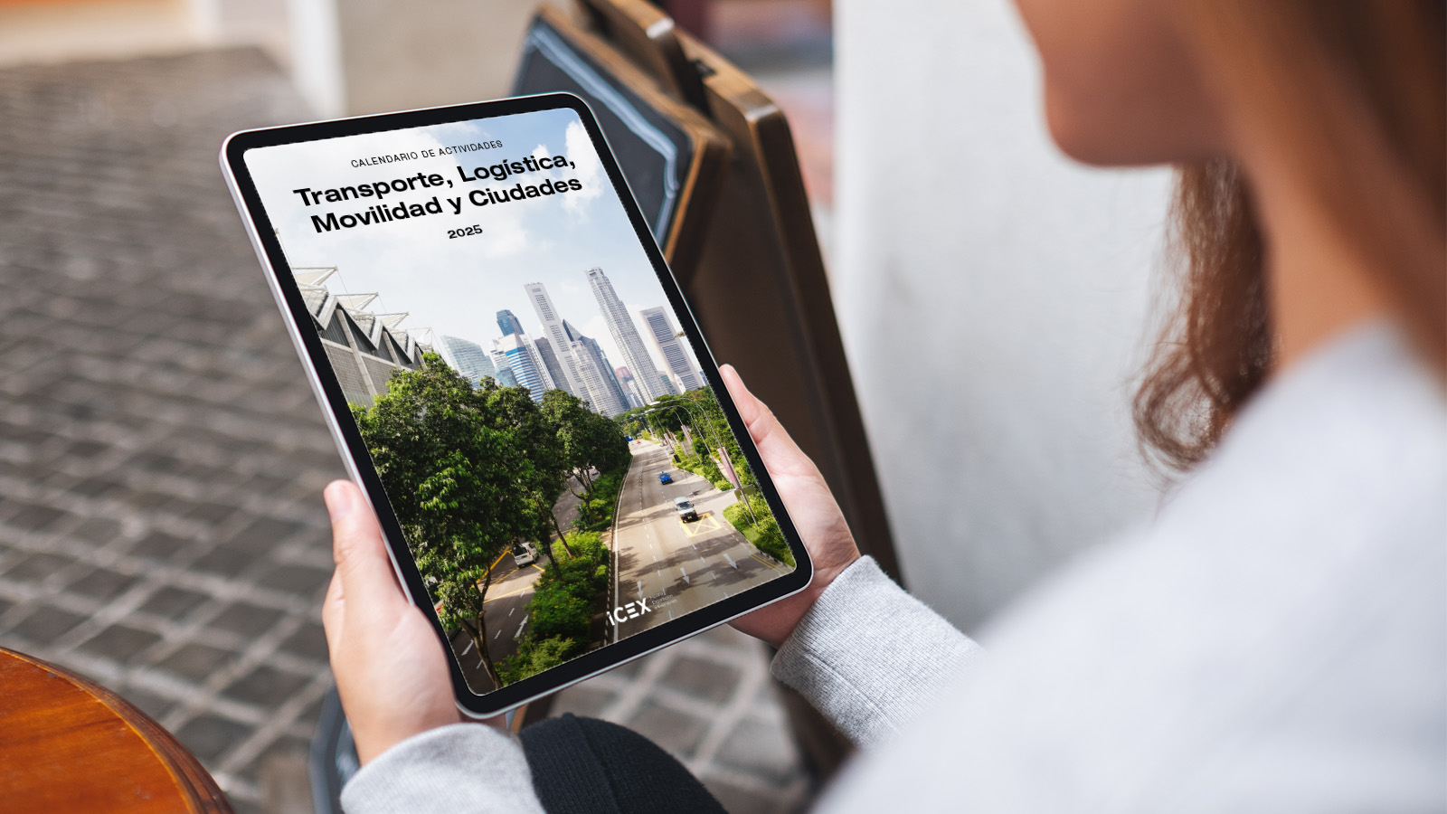 Una mujer sostiene con las dos manos una tablet donde visualiza el calendario ICEX para el sector del transporte 2025