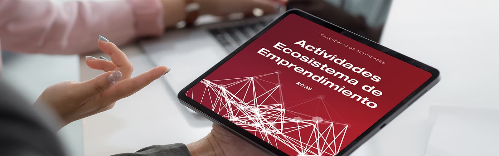 Una persona sujeta una tablet donde visualiza la portada del calendario de actividades para el sector emprendimiento tecnológico e innovador 2025