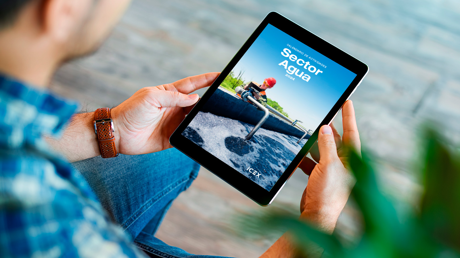 Una persona sujeta una tablet visualizando la portada del calendario de actividades del sector agua, ICEX