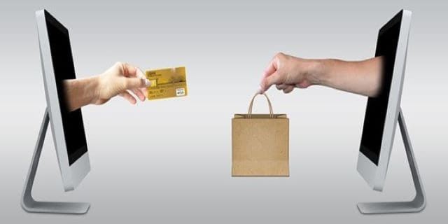 Dos manos saliendo de dos pantallas de ordenador con una bolsa y una tarjeta de crédito