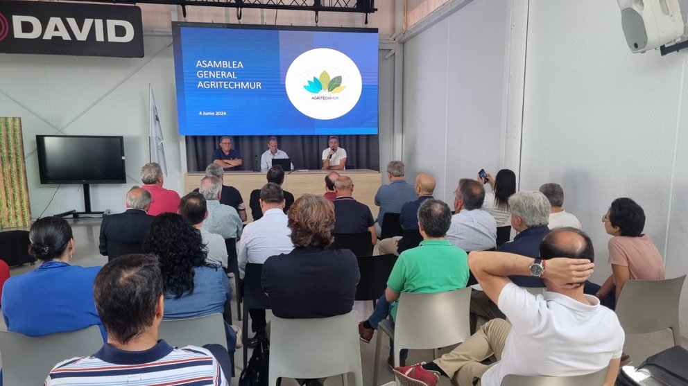 Varias personas sentadas escuchan a tres personas subidas a un escenario que protagonizan la asamblea de AgritechMurcia 2024.