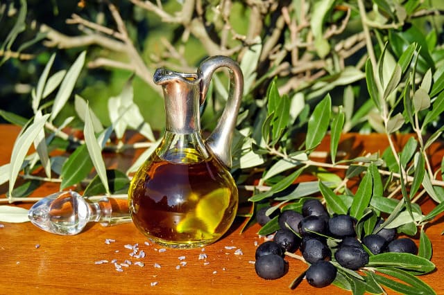 Botella de cristal con aceite de oliva rodeada de ramas de oliva