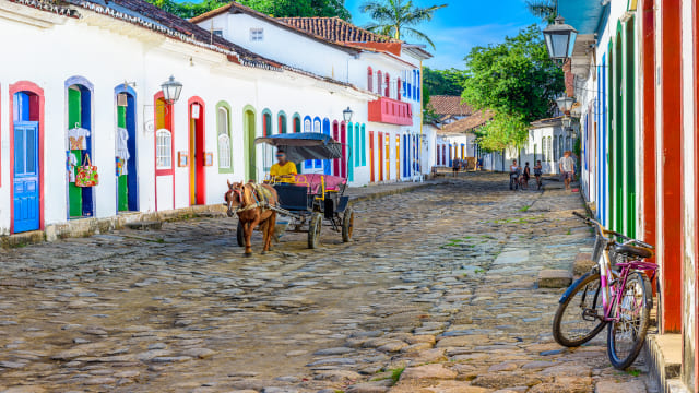 Calle empedrada con un carro con un caballo y fachadas de casas blancas con bordes de colores