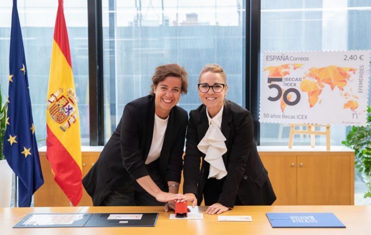 Dos personas sujentando un matasellos sobre una mesa y dos banderas de fondo