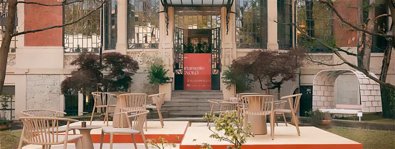 Una calle emblemática de Milán con edificios de fachada clásica blanca con los bordes de las puertas decorados con plantas y luces.