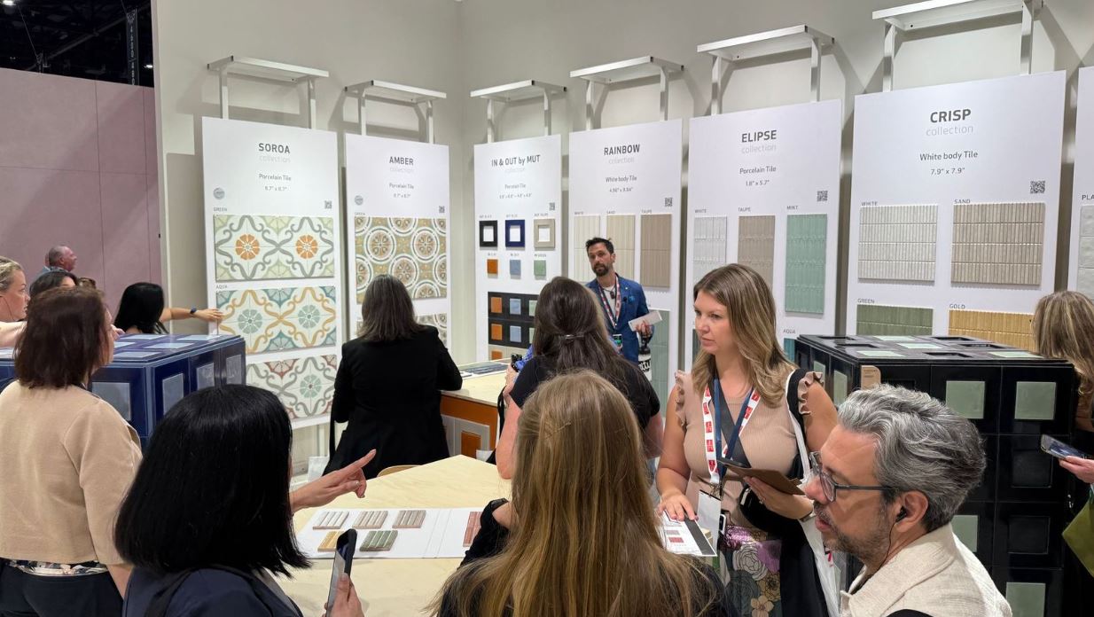 Un expositor está reunido con varios posibles clientes en una mesa, enseñándoles muestras. Detrás, otro expositor exhibe muestras con varios visitantes observando.