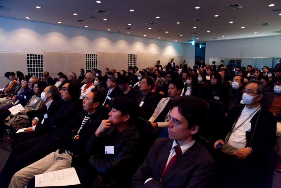 Varios visitantes japoneses e internacionales están sentados en un auditorio atendiendo un seminario