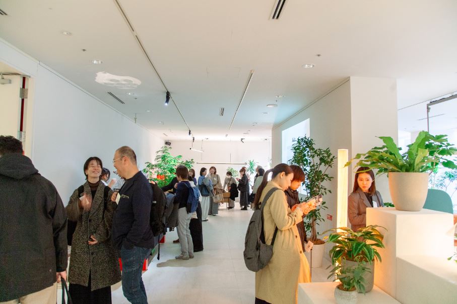 Varios visitantes japoneses observan las propuestas de diseño y mobiliario para interiores de las empresas españolas en un hall blanco