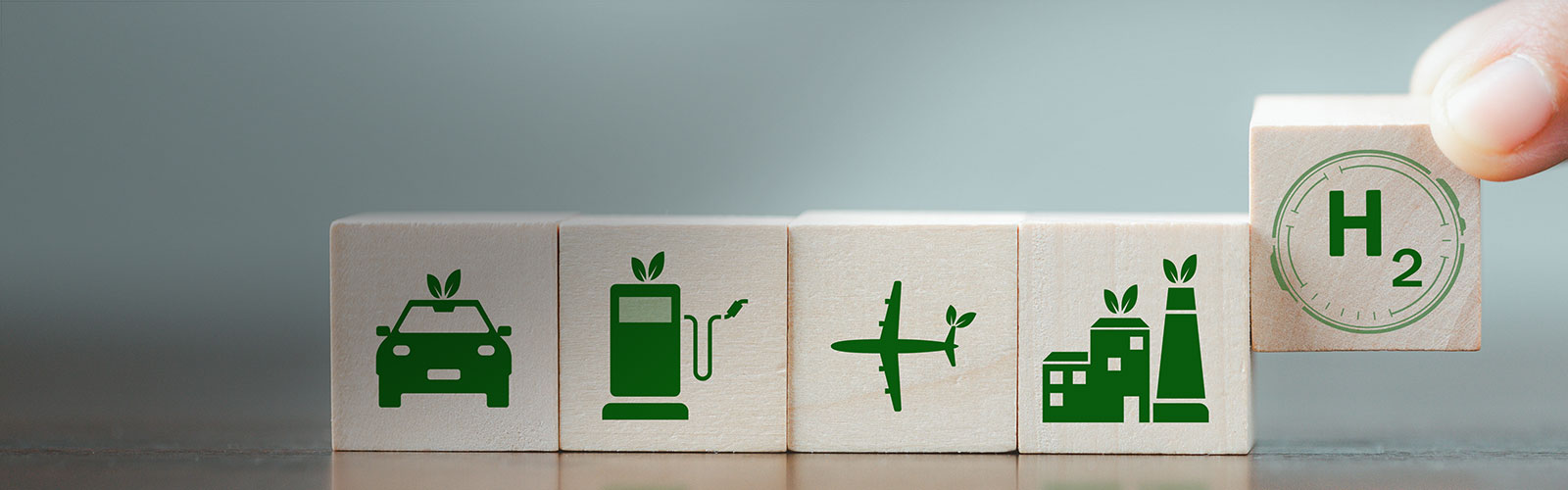 Cinco dados blancos, cada uno con un logo verde (un coche, un surtidor, un avión, unas casas y la fórmula química del hidrógeno) 