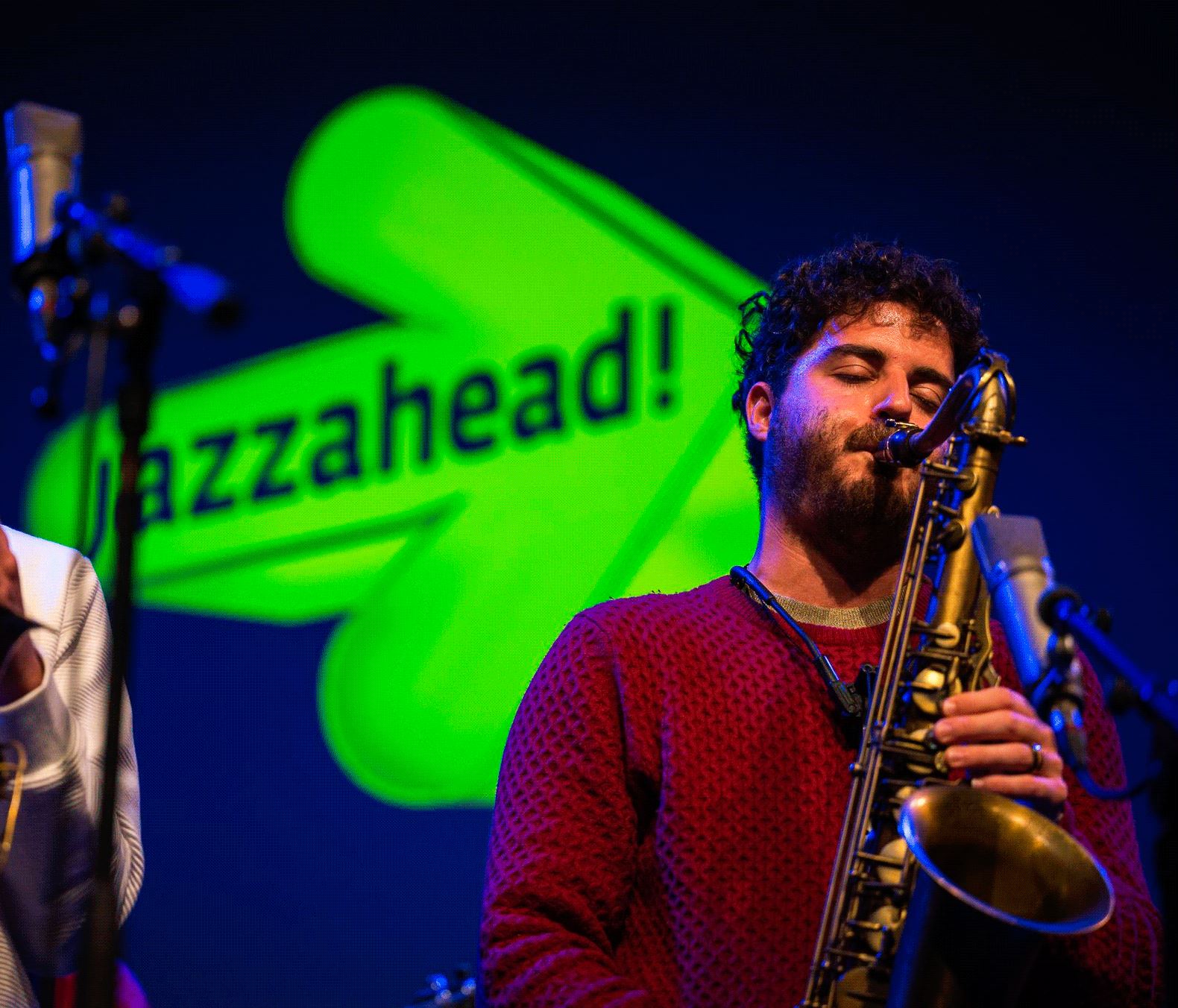 Un saxofonista toca el saxofón, al fondo se ve el icono verde de jazzahead!