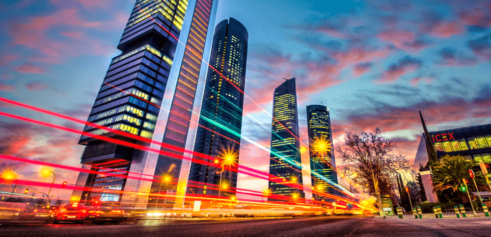 Las 4 torres de Madrid y la sede de ICEX, entre medias, en la carretera, se ven varios haces de luz rojos y verdes.