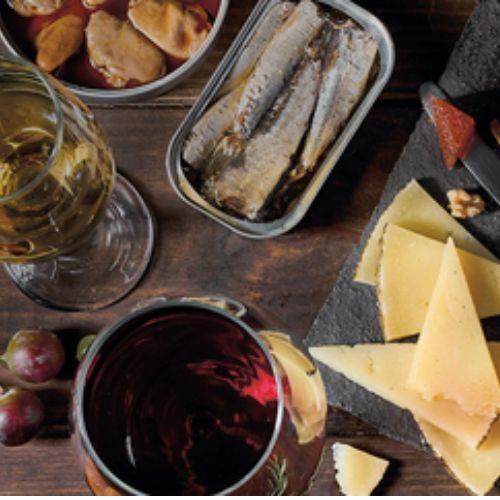 Cotillón que incluye cuñas de queso, una lata de sardinas, dos copas de vino blanco y tinto y otros alimentos.