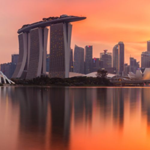 Tras el mar, se observa un skyline con los edificios más emblemáticos de Singapur al atardecer.