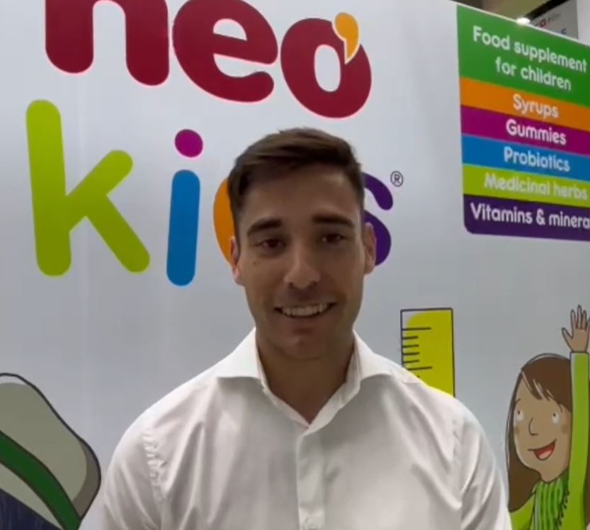 Hombre de pelo corto sonriente con camisa corta posa delante de un mural que anuncia nutracéuticos para niños