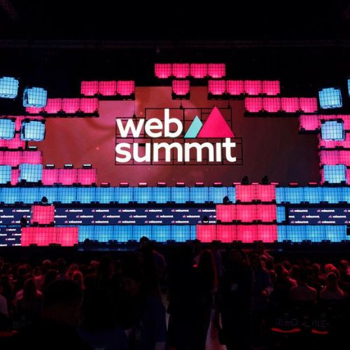 Escenario de conferencias de Web Summit Qatar iluminado con luces rosas y azules.