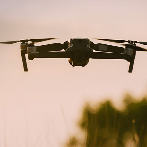 Un dron cuadricóptero vuela en un cielo de color cobrizo.