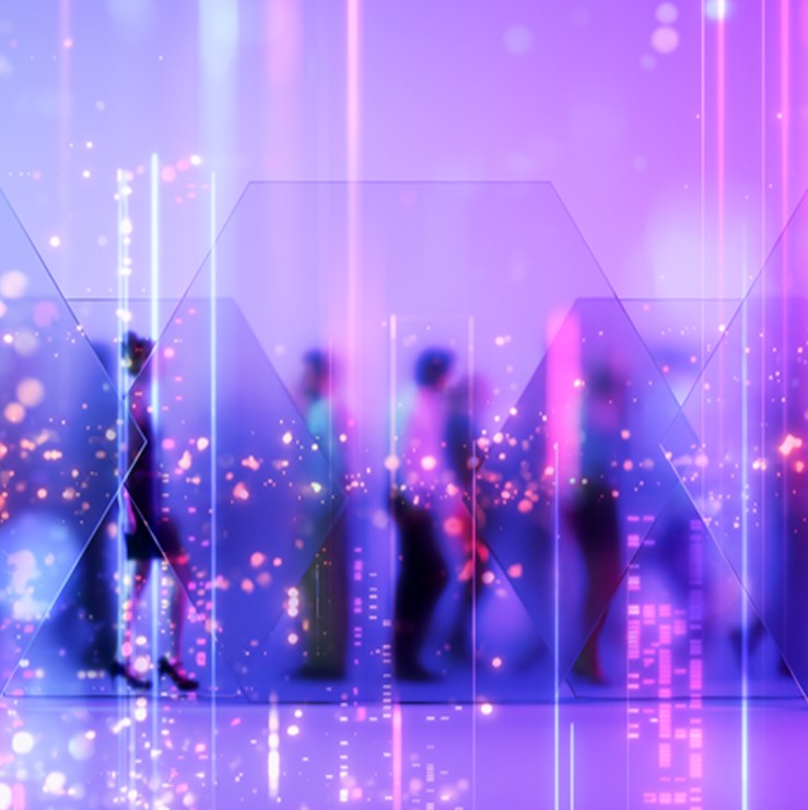 Varias sombras de personas están andando detrás de unos hologramas con filtros morados, rosas y azules; es una imagen conceptual que representa el carácter tecnológico de la feria.