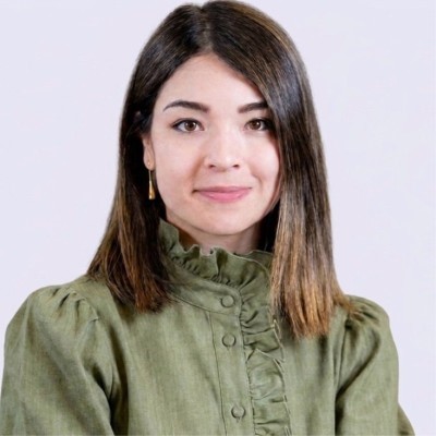 Retrato en primer plano de una persona con cabello liso a la altura de los hombros, vestida con blusa verde con cuello alto y detalles fruncidos. Fondo neutro claro e iluminación uniforme que resalta el rostro.