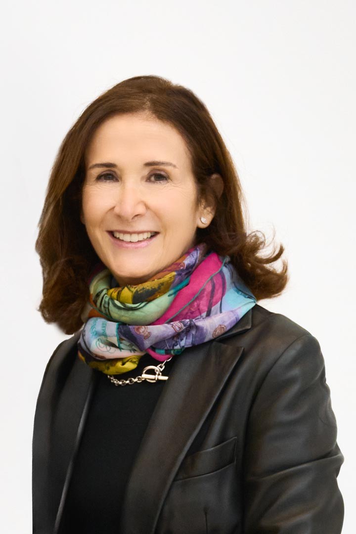 Mujer sonriente con chaqueta negra y pañuelo multicolor en retrato corporativo sobre fondo claro.
