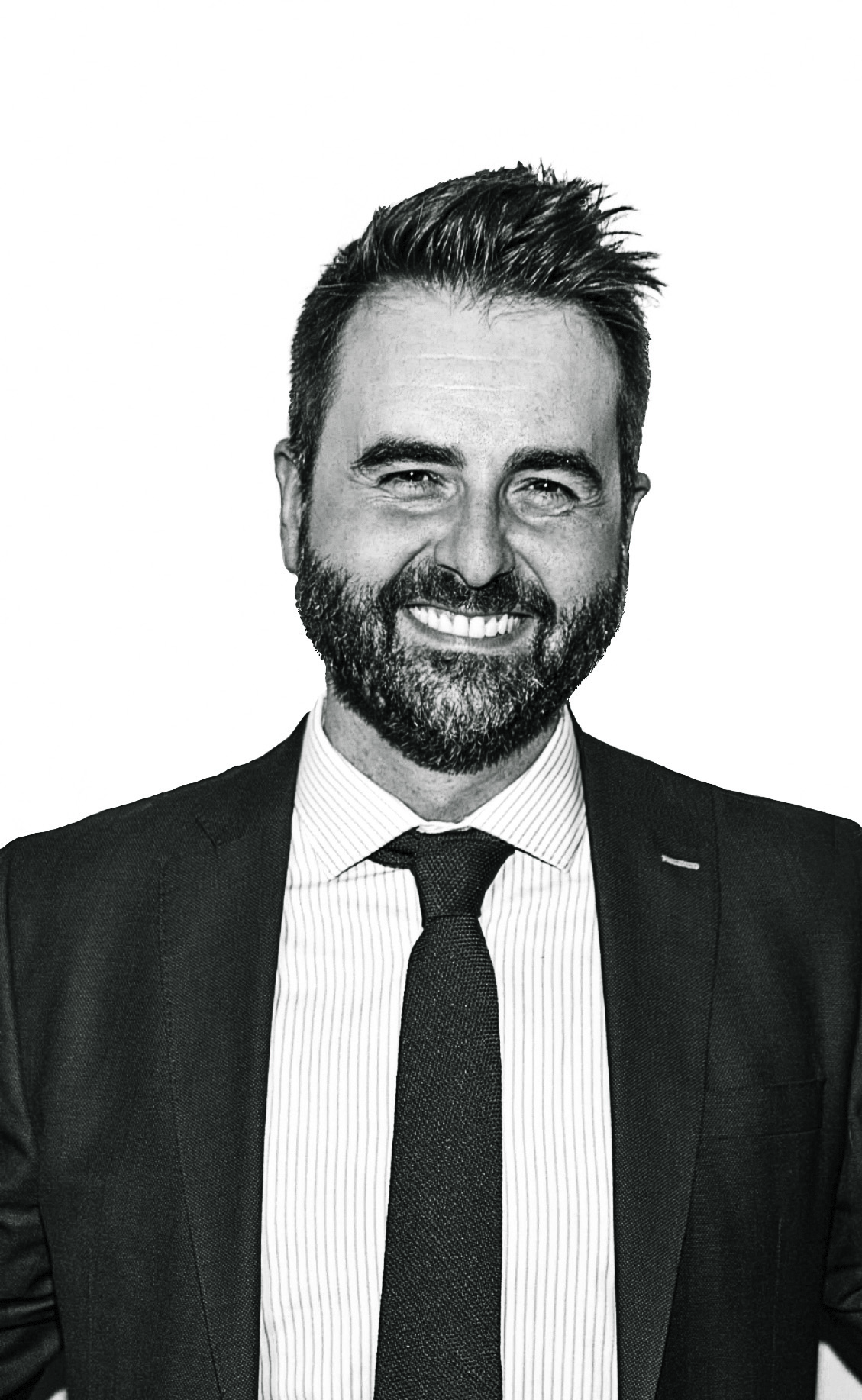 Hombre sonriente con barba, traje oscuro y corbata negra en retrato corporativo en blanco y negro.