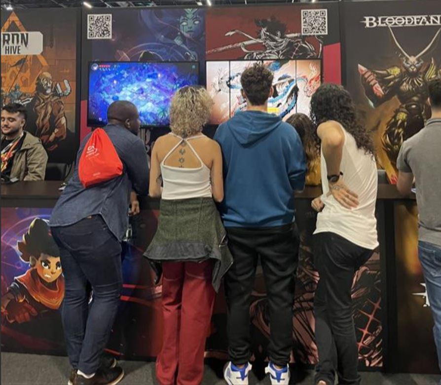 Cuatro gamers observan un proyecto de videojuego en un puesto de juego.