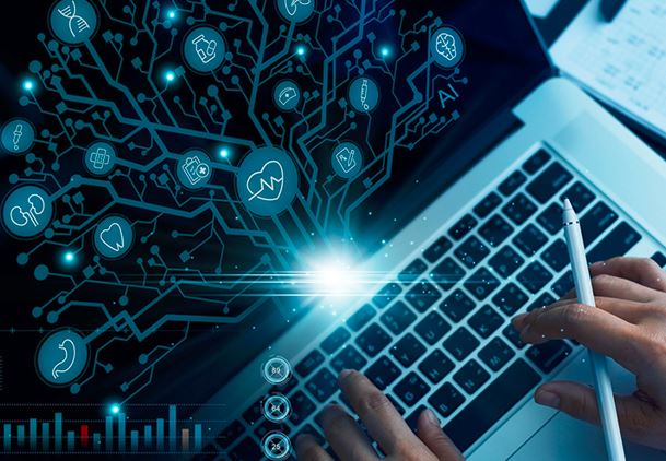 Unas manos teclean un ordenador de cuya pantalla salen hologramas con logos relacionados con el sector sanitario.