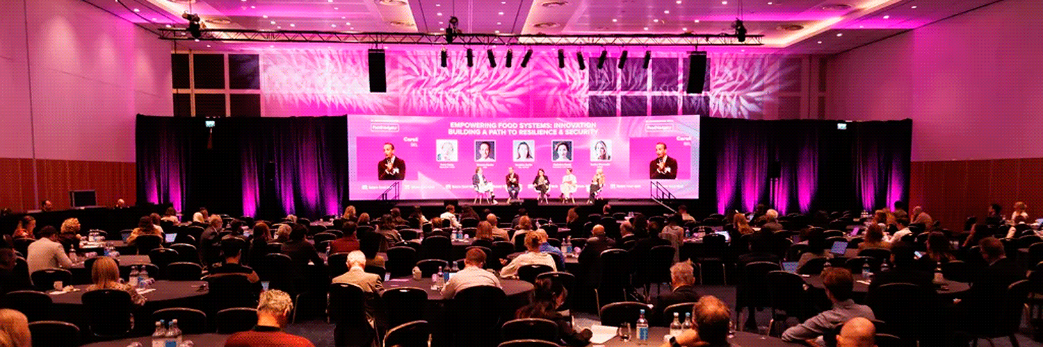 Cientos de asistentes sentados en mesas están viendo una mesa redonda donde expertos conversan sobre las innovaciones en el sector foodtech.