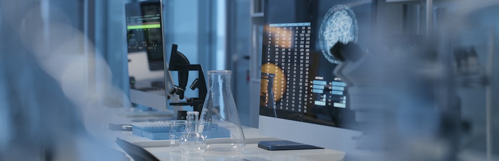 Una mesa con un ordenador con una interfaz de datos médicos, y dos tipos diferentes de microscopios a los dos lados.
