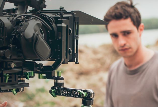 Una cámara enfoca a un actor con cara triste que viste una camiseta marrón.