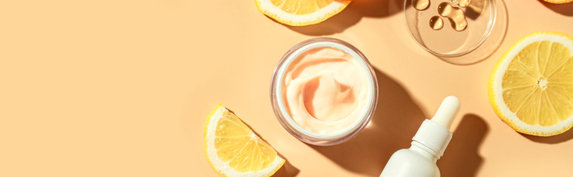 Un bote de unguento cosmético de color rosa junto a varios limones y un bote blanco con un cuentagotas.