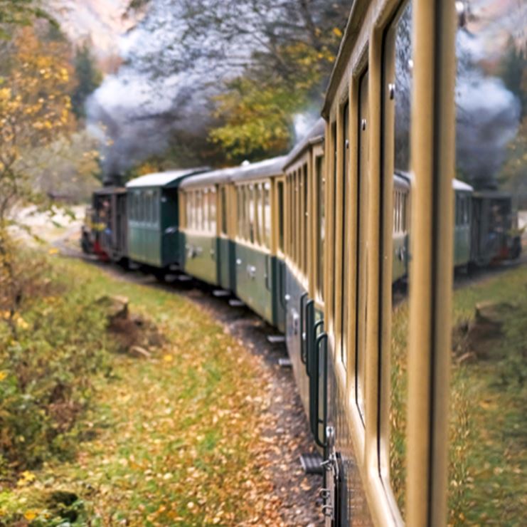 Un tren clásico recorre un camino al lado de un bosque con árboles de hojas amarillas en una estampa otoñal.