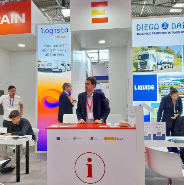 Un representante de una empresa española está de pie detrás del mostrador de su puesto de trabajo en el Pabellón España de Transport Logistic.
