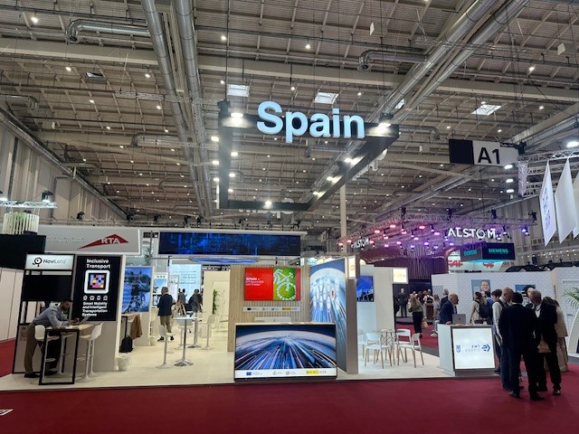 Panorámica del Pabellón España de UITP Summit Alemania con todos sus stands y varios profesionales visitándolos.