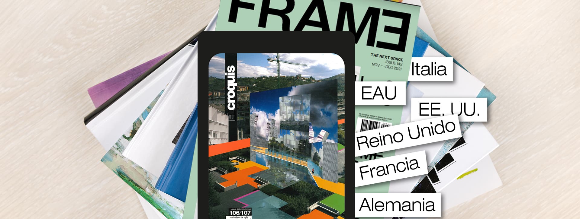 Un móvil que reproduce un collage de revistas de hábitat. Detrás hay varias revistas acumuladas y unas etiquetas donde pone "Italia", "EAU", "EE. UU.", "Reino Unido", "Francia" y "Alemania".