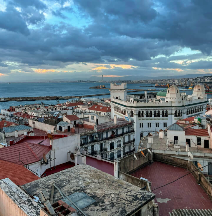 Vista de Argel al atardecer, con edificios de arquitectura colonial, techos rojos y el mar Mediterráneo de fondo