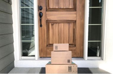 Imagen ilustrativa para la noticia de cómo identificar un catálogo ganador para vender en Amazon fuera de España. Presenta varias cajas de reparto frente a la puerta de un domicilio..