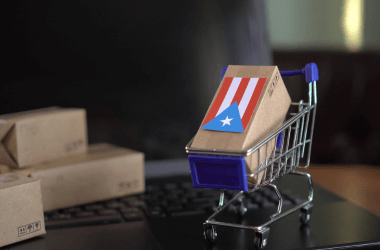 Imagen de una caja de paquetería con la bandera de Puerto Rico, dentro de un carro de supermercado