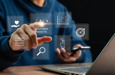 Imagen ilustrativa para la noticia de la personalización y la relación con el cliente, claves del comercio digital en Colombia en 2026. Muestra una persona pulsado un botón holográfico frente a un ordenador, con un móvil en la mano.