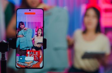 Imagen ilustrativa para la noticia de Comercio Digital, la consolidación del live commerce en Asia marca una nueva era para el ecommerce global. Muestra dos chicas fuera de foco grabándose con un móvil abriendo compras.