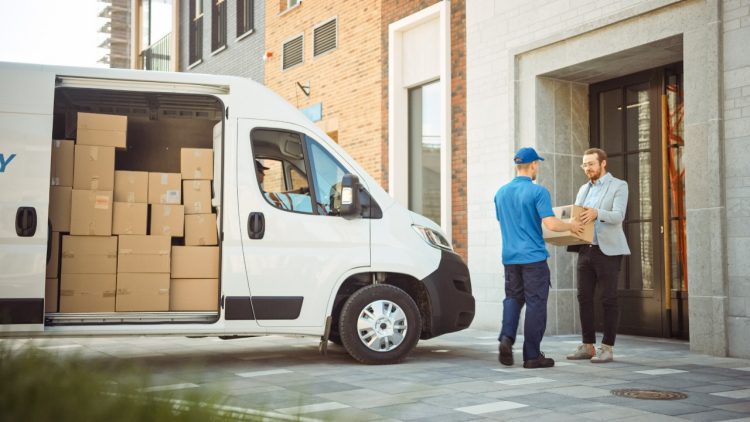 Imagen ilustrativa para la noticia "Cómo el e-commerce redefine la logística urbana en EE. UU.". Muestra a un repartidor junto a una furgoneta de reparto entregando un paquete a un hombre en el portal de su casa.
