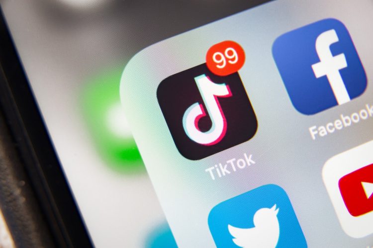 Imagen ilustrativa para la noticia "TikTok Shop aterriza en Bélgica: nace un nuevo canal de social commerce". Muestra un plano detalle de una pantalla de móvil centrado en el icono de la aplicación TikTok con 99 notificaciones.