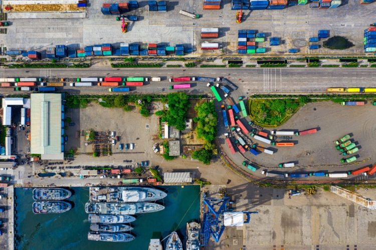 Imagen ilustrativa para la noticia "Los costes logísticos condicionan las compras online de los portugueses". Muestra un plano cenital de camiones de carga y barcos en un puerto.