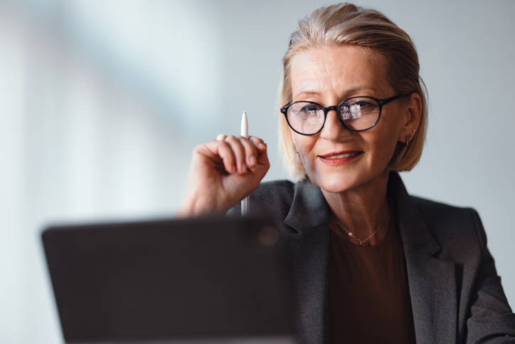 Primer plano de una elegante mujer de negocios senior, sentada en el escritorio de la oficina y usando su tableta digital para trabajar.
