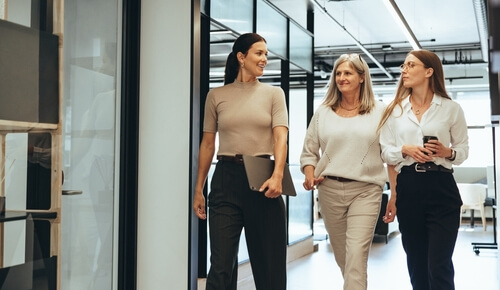 tres mujeres hablan sonrientes andando por el pasillo de la oficina